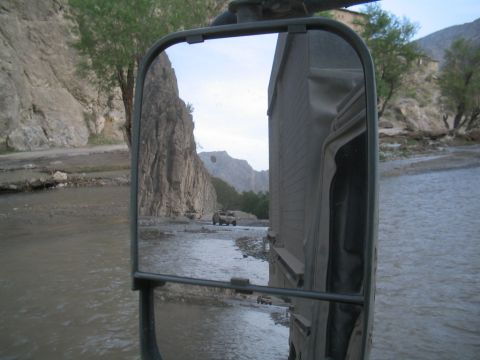 1981 Ford Bronco - A convoy of military vehicles navigates a shallow riverbed, with steep, rocky cliffs lining the path.