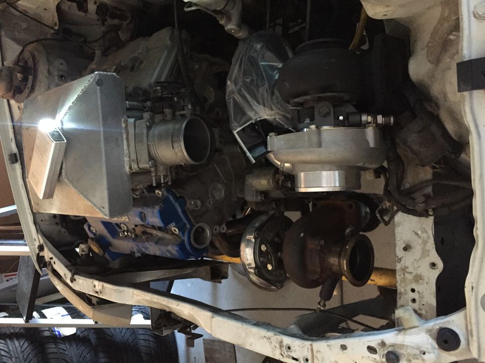 Engine bay with twin turbochargers, intercooler, and intake manifold. White vehicle frame visible