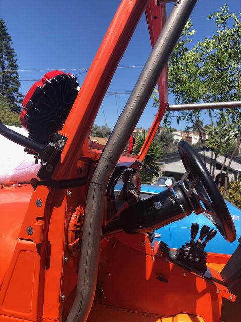 1992 Jeep Wrangler - Detail of an orange off-road vehicle showing tube roll cage, steering wheel, shifter and a red snorkel air intake under blue sky.
