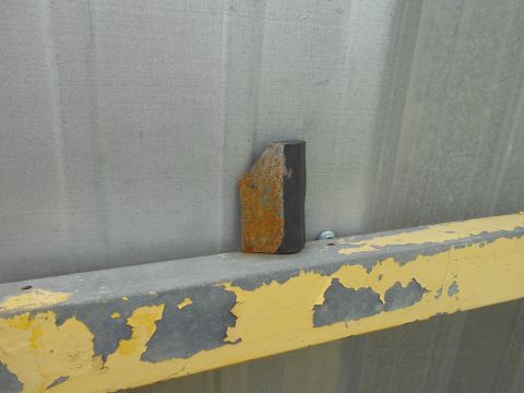 1992 Ford Bronco - A rusted metal part sits on a beam with peeling yellow paint.