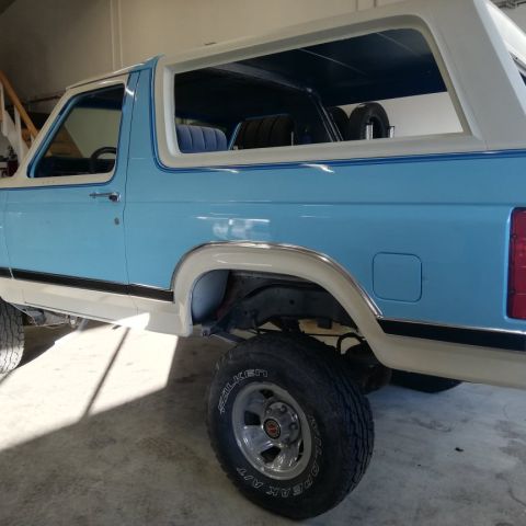1996 Ford Bronco - This 1980s Ford Bronco features a two-tone paint scheme and a spare tire visible through the rear window.