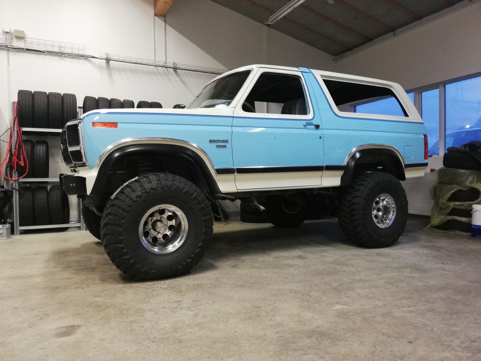 Light blue and white Ford Bronco with lifted suspension and large tires parked indoors