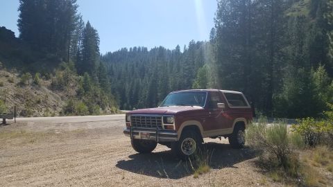 1985 Ford Bronco - 1985 Ford Bronco parked off-road with a scenic mountain backdrop.
