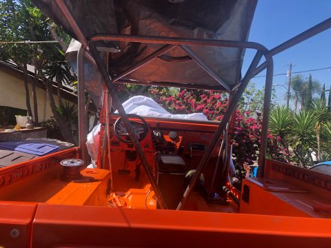 1992 Jeep Wrangler - The interior of an orange Jeep Wrangler is shown, featuring a roll cage and a partially covered dashboard. The vehicle is parked outdoors w…