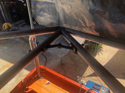 1992 Jeep Wrangler - A metal roll cage structure is being assembled over the orange bed of a vehicle. The structure is made of dark metal tubing and is partiall…