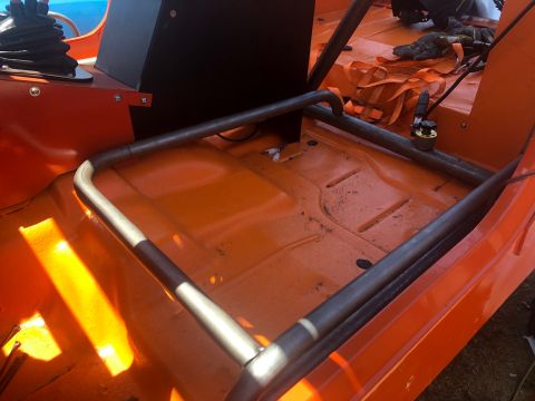 1992 Jeep Wrangler - The interior of an orange Jeep Wrangler shows a roll cage structure over the floorboards. Straps and gloves are visible in the background.