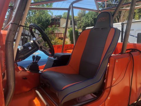 1992 Jeep Wrangler - Interior view of an off-road vehicle's driver's side, featuring an orange exterior, a PRP racing seat with grey and orange upholstery, and…