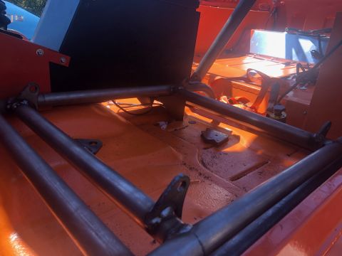 1992 Jeep Wrangler - The interior of an orange vehicle shows a custom roll cage welded to the floor. A black box and orange seat belts are visible in the backgr…