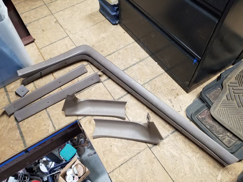 Several tan interior trim pieces, including a long piece and two curved pieces, laid out on a wooden floor
