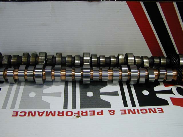 Two camshafts with copper and silver bearings on a box with text