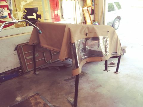 1996 Ford Bronco - A tan canvas soft top with clear plastic windows is draped over a metal frame in a garage. A blue hydraulic jack is visible on the floor to…