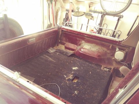 1996 Ford Bronco - The interior of a vintage pickup truck bed, showing the worn black matting and maroon painted sides. Tools and a bicycle are visible in the…