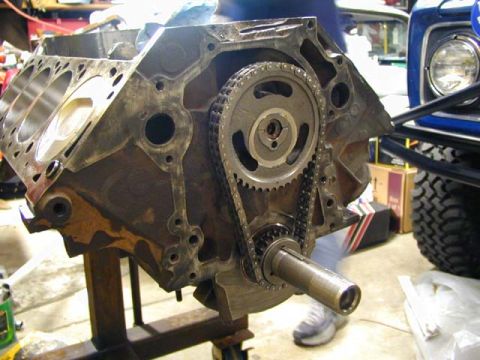 1979 Ford Bronco - Engine block assembly with timing chain and gears, next to a blue vehicle.