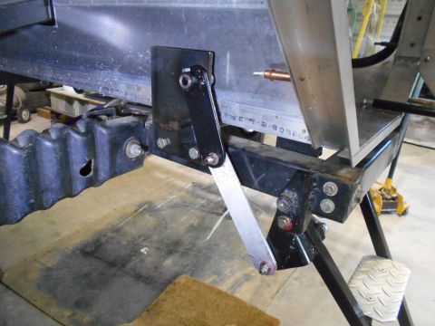 1992 Ford Bronco - A close-up view of a mechanical linkage attached to a black frame and a ribbed black component, likely part of a vehicle's suspension or un…