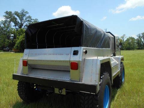 1992 Ford Bronco - Rear 3/4 view of a custom utility truck with a black canvas top, parked in a grassy field under a blue sky.