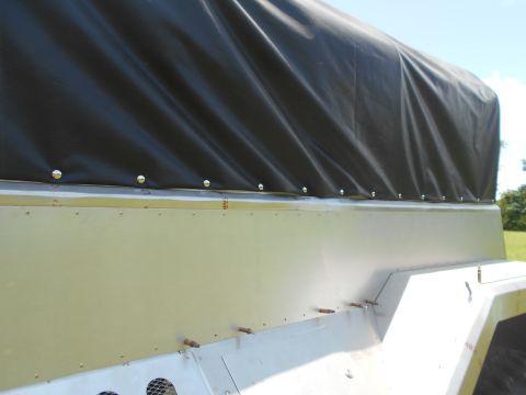 1992 Ford Bronco - A close-up, side view of a trailer bed with a black tarp covering the top. The trailer bed is light tan and has visible rivets and fastener…
