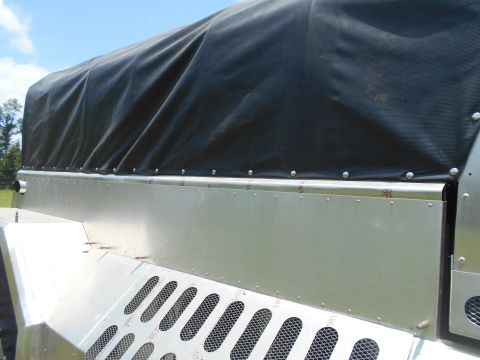 1992 Ford Bronco - A close-up view of the side of a trailer or truck bed, featuring a black tarp covering the top and a silver metal lower section with perfor…