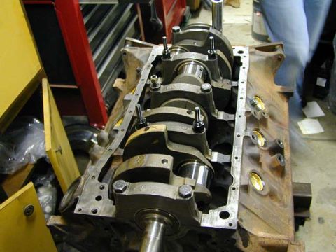 1979 Ford Bronco - Close-up of an engine block and crankshaft, with a person standing nearby in a workshop setting.