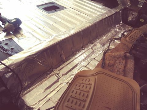 1996 Ford Bronco - The interior floor of a vehicle is being lined with sound deadening material. A power drill is visible on the left side of the frame.
