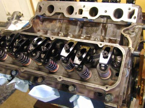 1979 Ford Bronco - Close-up of a V8 short block during assembly with a cylinder head bolted on, valve cover off, showing roller rocker arms on studs over dual…
