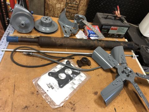 1978 Ford Bronco - A collection of automotive parts, including pulleys, a driveshaft, a fan, and a battery charger, are laid out on a workbench.