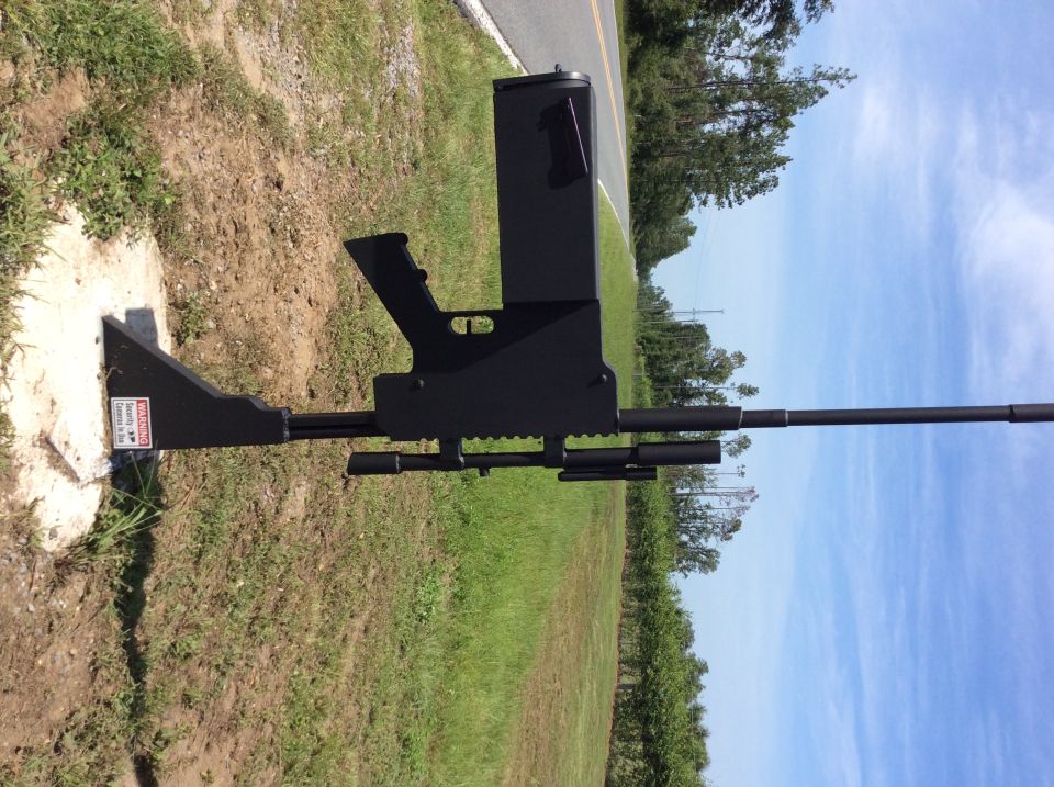 Black gun-shaped object mounted on a concrete base next to a road.