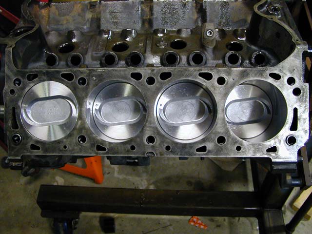 Engine block with four pistons visible, resting on a stand