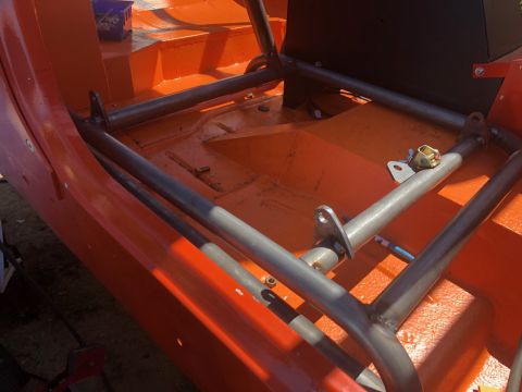 1992 Jeep Wrangler - The interior of an orange vehicle shows a custom metal roll cage being installed over the floor pan. Several mounting brackets are welded t…