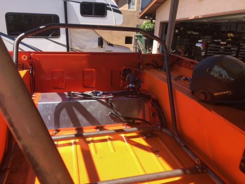 1992 Jeep Wrangler - The interior of a custom off-road vehicle, likely a Jeep, shows an orange-painted bed with a silver fuel tank and a roll cage. A black helm…
