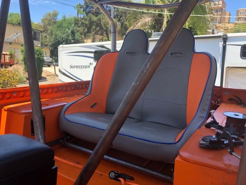 1992 Jeep Wrangler - The interior of an orange off-road vehicle shows two grey and orange bucket seats with blue piping, surrounded by a metal roll cage. A whit…