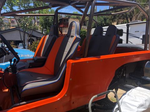 1992 Jeep Wrangler - The interior of an orange Jeep Wrangler features custom racing seats with orange, grey, and blue accents. A roll cage is visible overhead,…