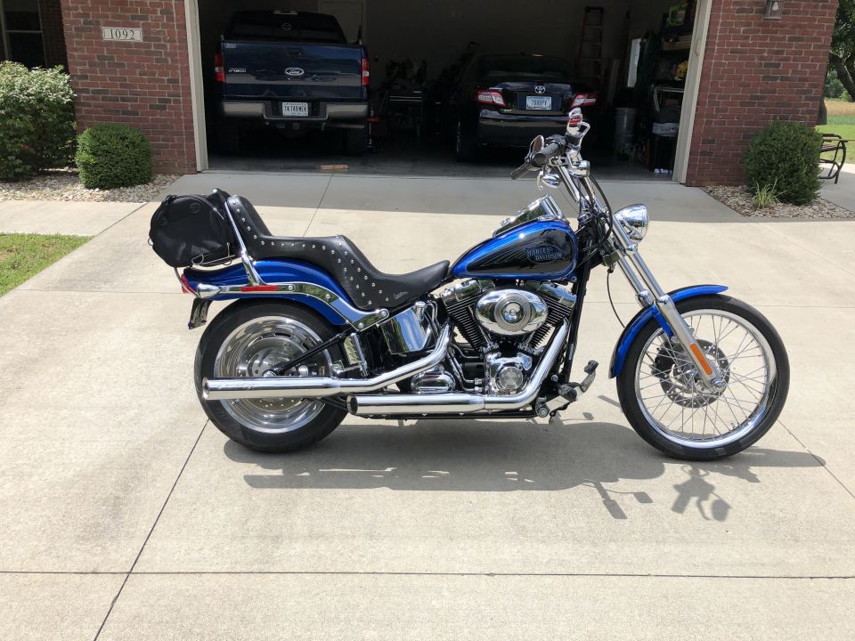 Blue Harley-Davidson Softail motorcycle with black studded seat and saddlebag parked in front of a garage.