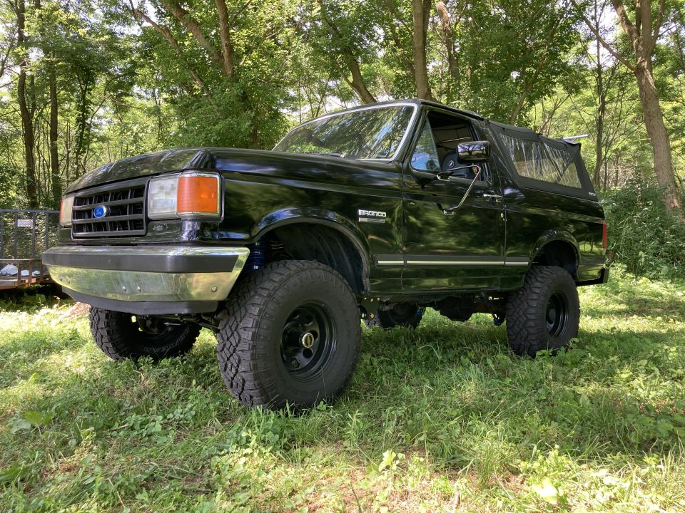 Black 1987 Ford Bronco with soft top and off-road tires parked outdoors.