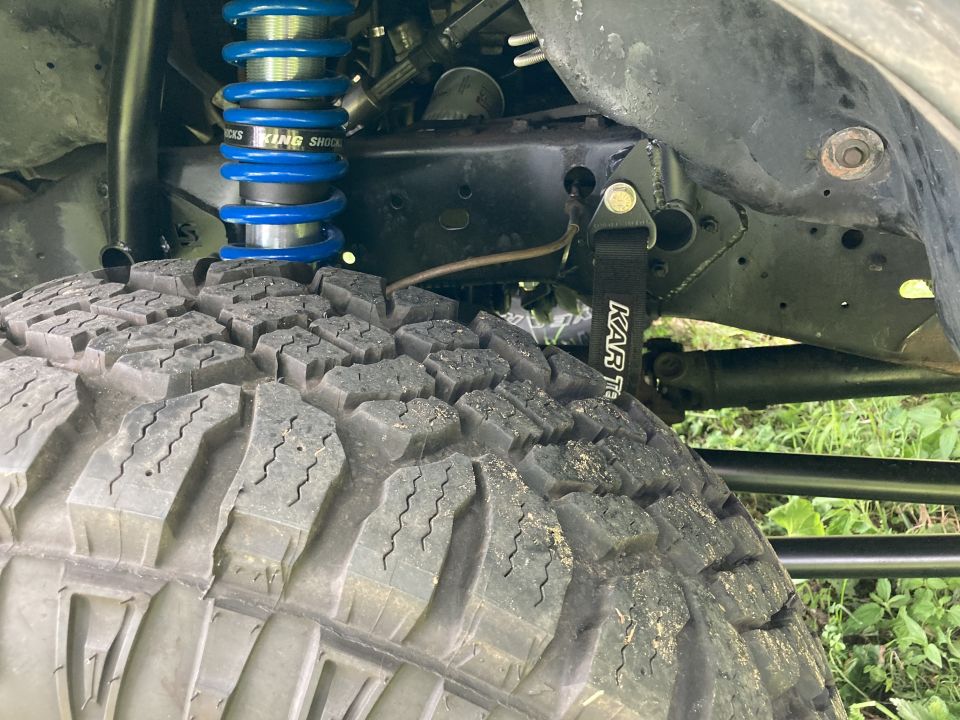 Close-up of off-road tire, blue King Shock, and black tow strap on a vehicle.