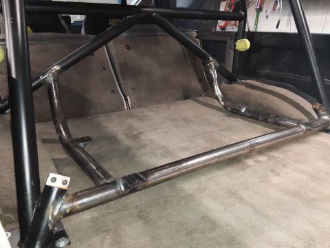 1985 Toyota Hilux - The interior of a vehicle shows a custom roll cage installed over the carpeted rear seating area. The roll cage is constructed from black a…