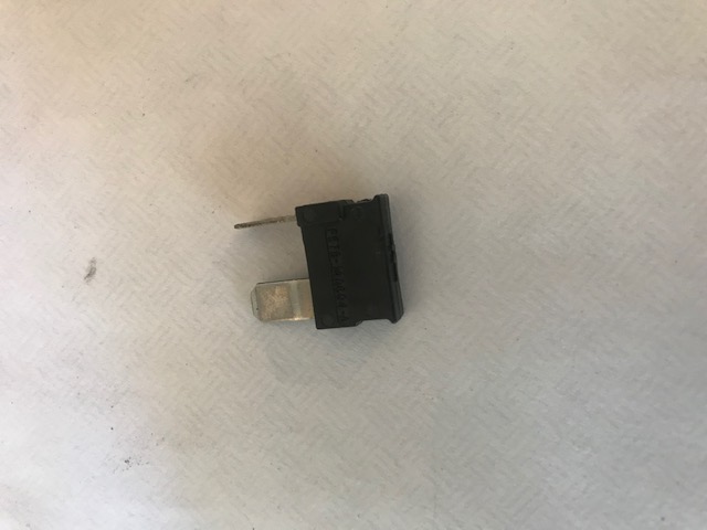 Black automotive fuse with metal prongs and visible text.