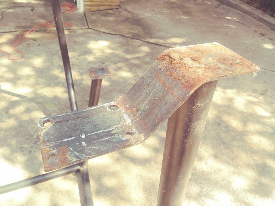 Rusted metal bracket with bolt holes attached to a black metal pole.