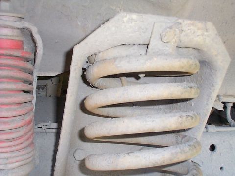 1979 Ford Bronco - Close-up of a front suspension coil spring and red shock absorber, likely from an older vehicle.