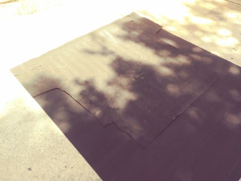 1996 Ford Bronco - A dark, flat material is laid out on a concrete surface, with dappled sunlight and shadows falling across it. The material appears to be so…