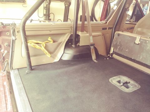 1996 Ford Bronco - The interior of a 1996 Ford Bronco shows the rear cargo area with black carpet and a tan interior trim. A yellow rope is coiled in a door p…