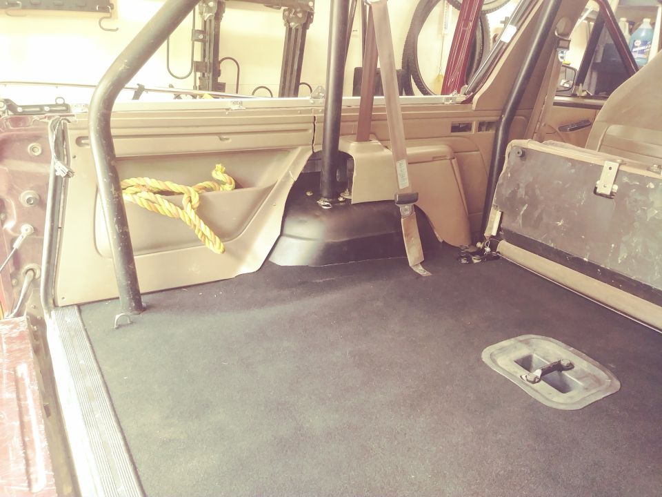 Interior rear cargo area of a 1996 Ford Bronco with black carpet and tan trim.