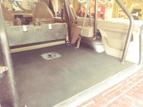 1996 Ford Bronco - The interior of a 1996 Ford Bronco is shown, focusing on the rear cargo area. The floor is covered in black carpet, and a metal storage box…