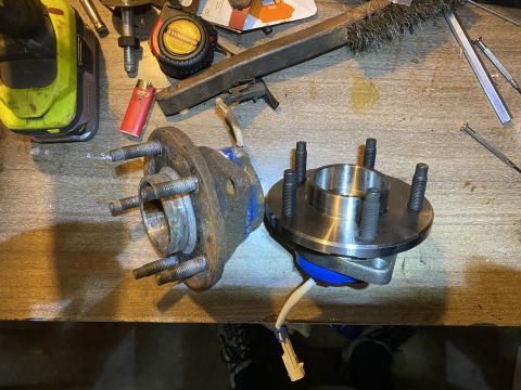 Old and new five-lug front wheel hub bearing assemblies on a workbench