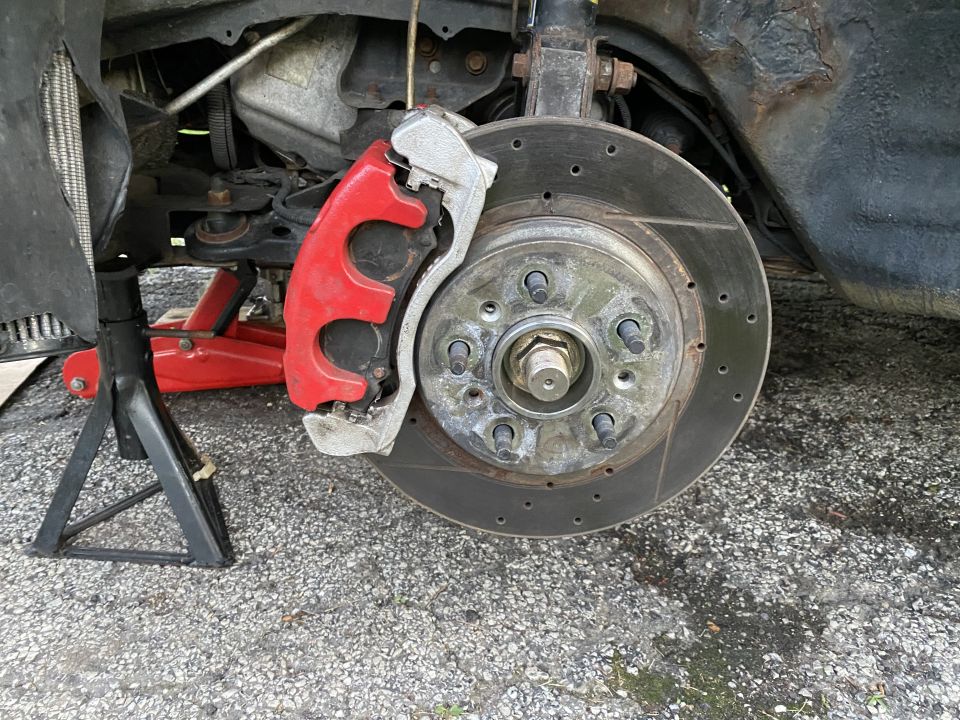 Front disc brake with red caliper and drilled slotted rotor on vehicle on jack stand
