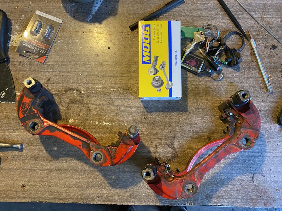 Two red suspension control arms on a workbench with a Moog parts box and keys.