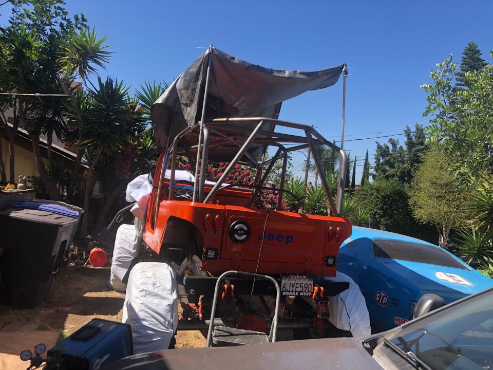 1992 Jeep Wrangler with custom roll cage and tarp, parked next to a blue car