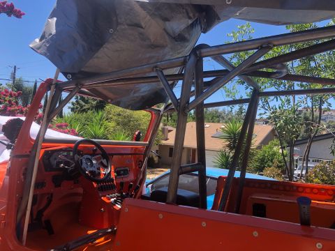 1992 Jeep Wrangler - The interior of an orange Jeep is shown with a custom roll cage structure and a tarp covering part of the roof.