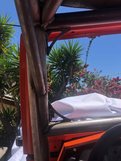 1992 Jeep Wrangler - Custom roll cage structure with orange interior panels and a white tarp visible against a bright blue sky and foliage.