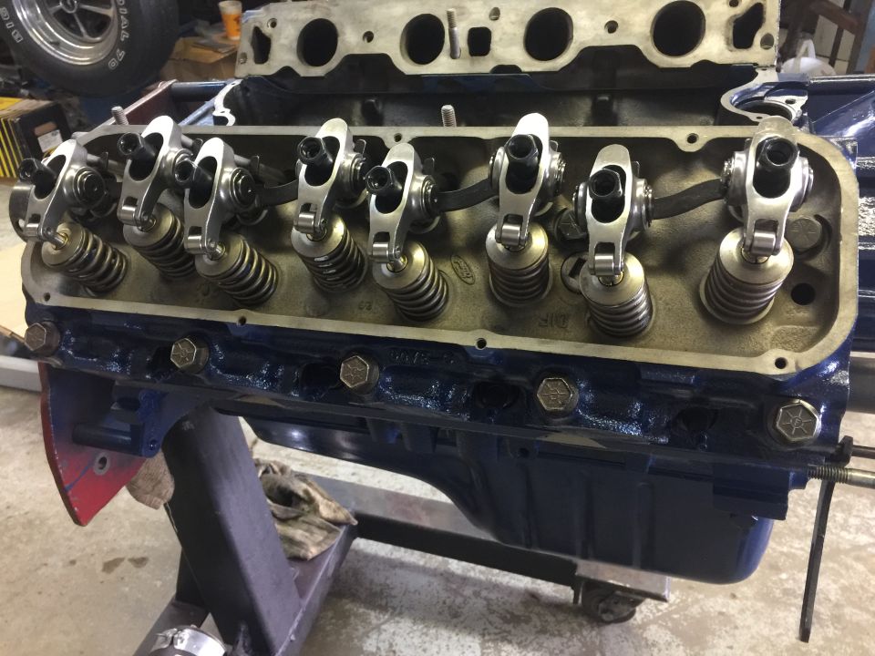 Blue Ford V8 engine block with silver rocker arms and springs, mounted on a stand