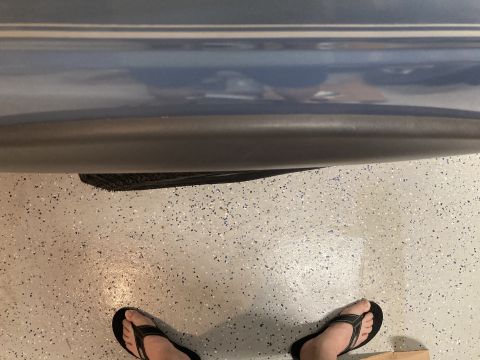 1998 Ford Ranger - A close-up shot shows the side of a vehicle, focusing on the lower body panel and a tire, with a person's feet in flip-flops on the garage…